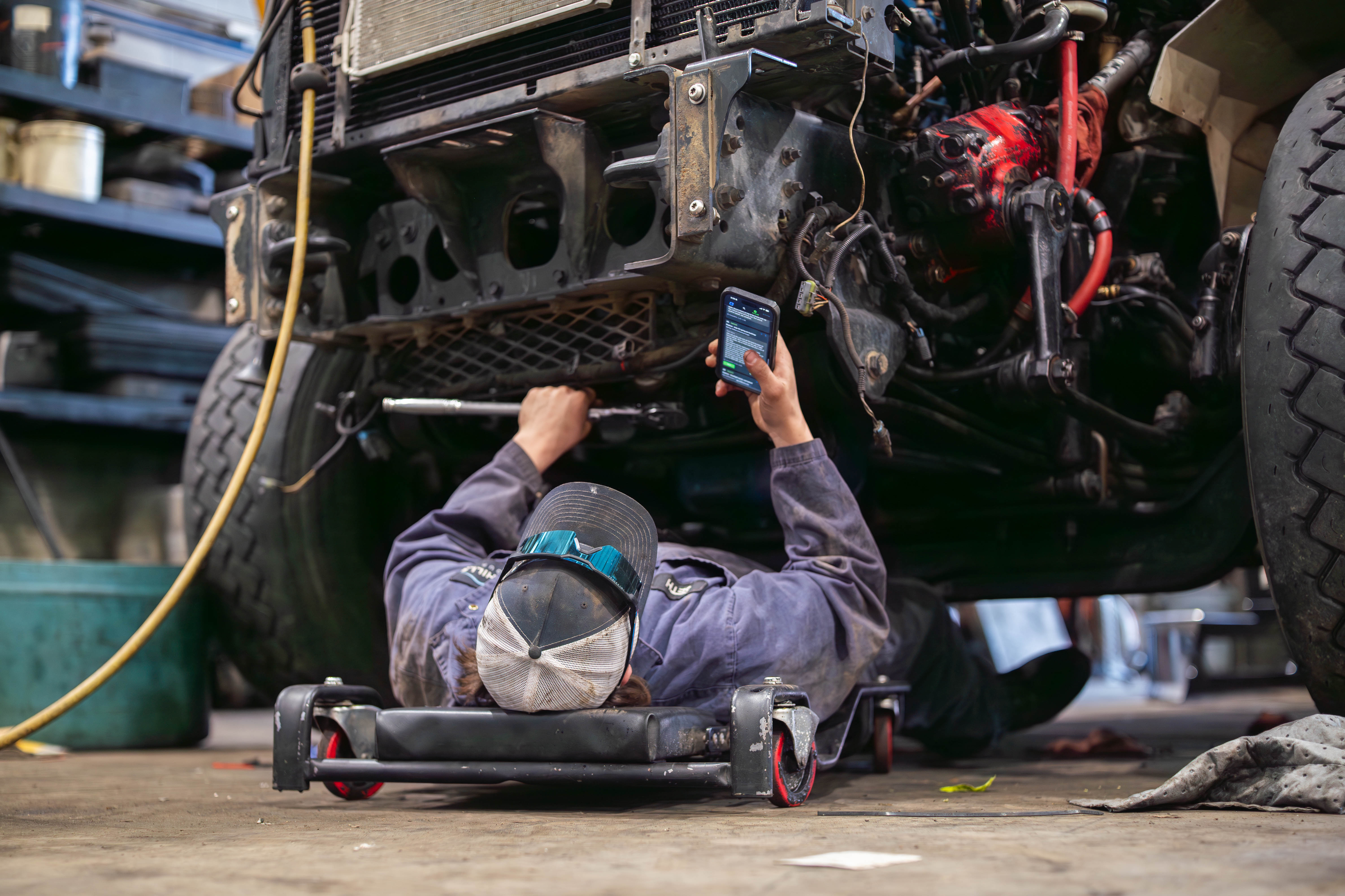 Technician using ShopView on mobile while working under a truck
